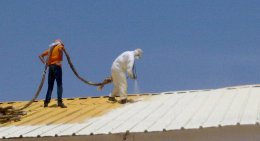 Dos aplicadores sobre un tejado proyectando espuma de poliuretano